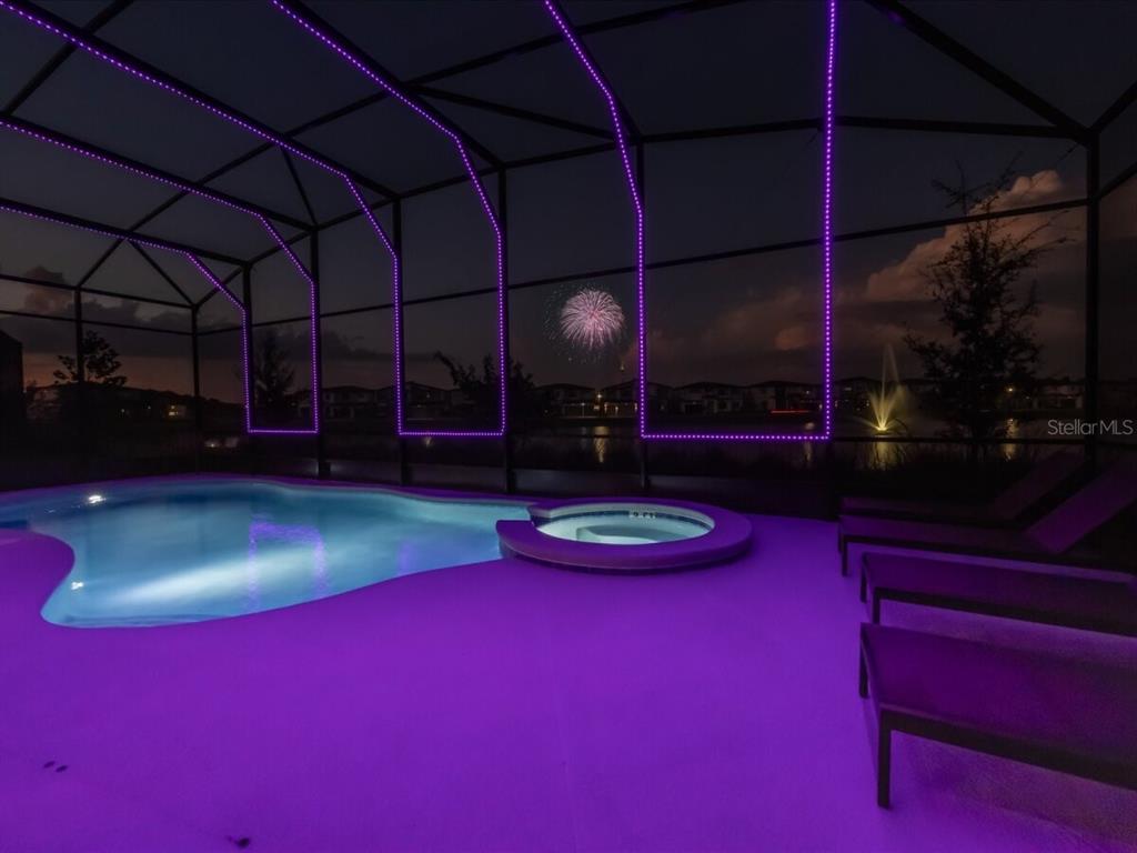 A swimming pool and spa inside a screened enclosure at night with purple accent lighting — 5830 HIGH SEAS DRIVE, ORLANDO, FL