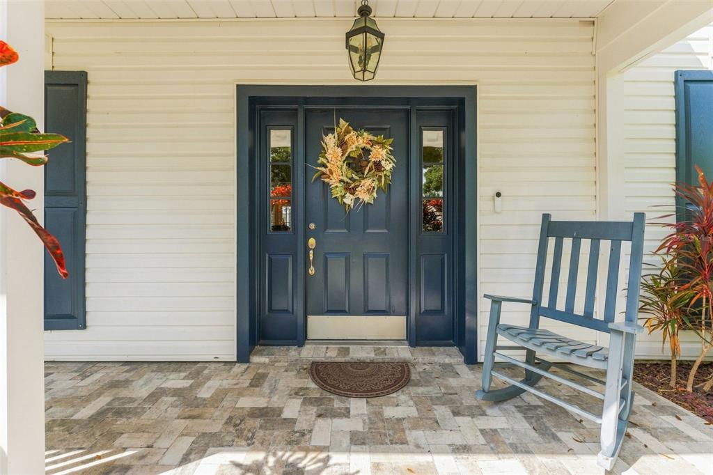 A front porch with a blue door, a rocking chair, and stone paver flooring — 15622 INDIAN QUEEN DRIVE, ODESSA, FL