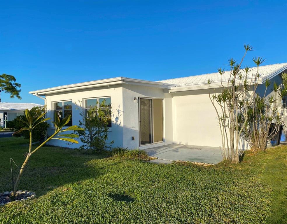 The exterior of a white house features a concrete patio, sliding glass doors, and landscaping — 10032 36TH STREET N, PINELLAS PARK, FL
