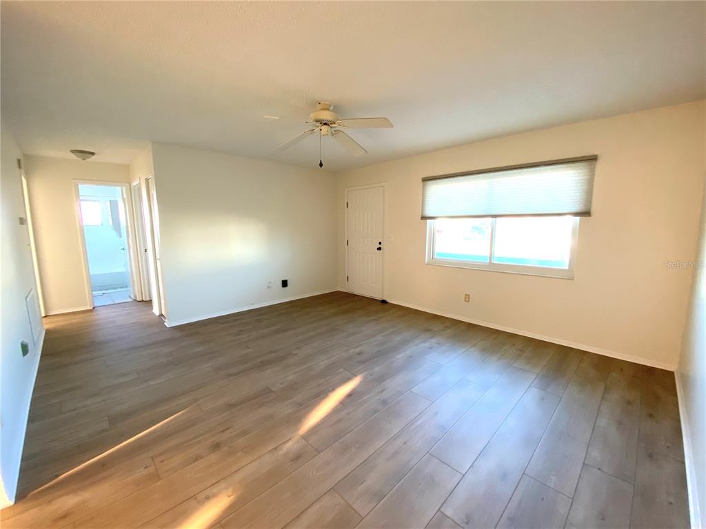 An empty living room features light wood-look flooring, a ceiling fan, and a white door — 10032 36TH STREET N, PINELLAS PARK, FL