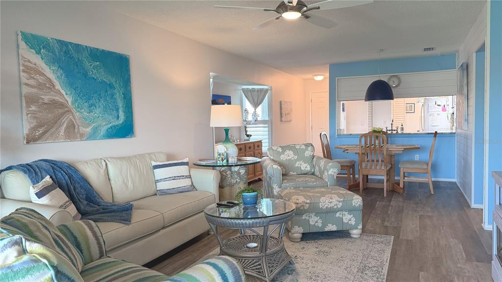 A living room with a sofa, floral armchair, glass coffee table, and adjacent dining area — 7163 28TH AVENUE W UNIT 7163, BRADENTON, FL