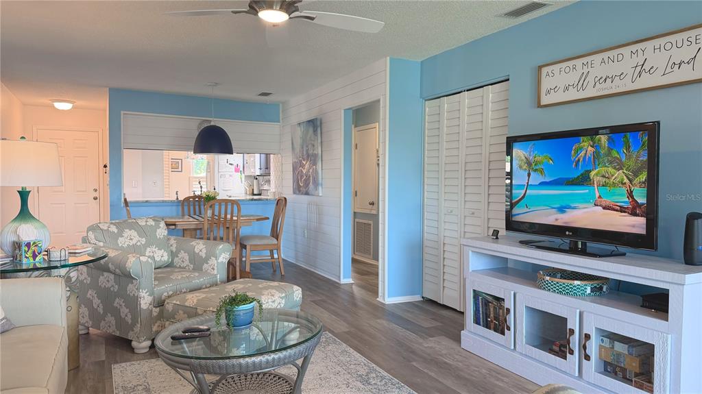 A living room with light blue walls, a television, a floral armchair, and a dining area — 7163 28TH AVENUE W UNIT 7163, BRADENTON, FL