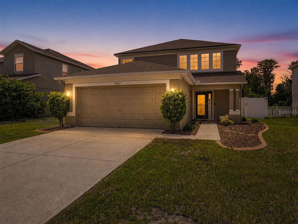 A two-story suburban house with a tan exterior, a two-car garage, and a concrete driveway — 12607 CHENWOOD AVENUE, HUDSON, FL