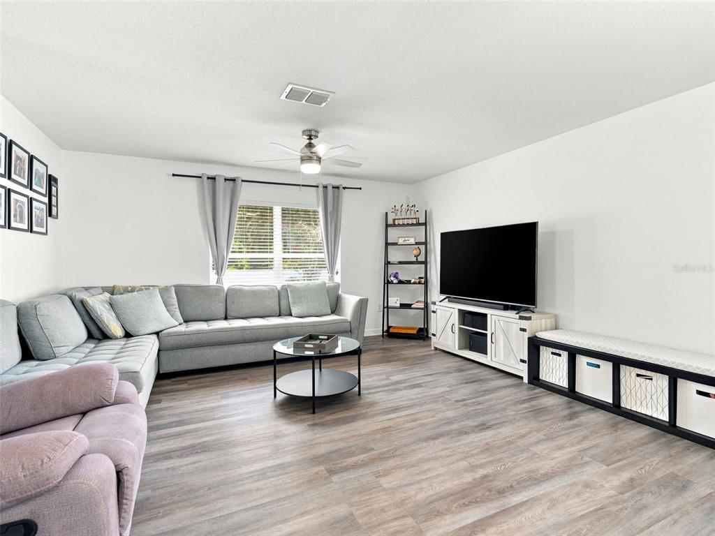 A living room features a grey sectional sofa, a television on a console, and wood-look flooring — 12607 CHENWOOD AVENUE, HUDSON, FL