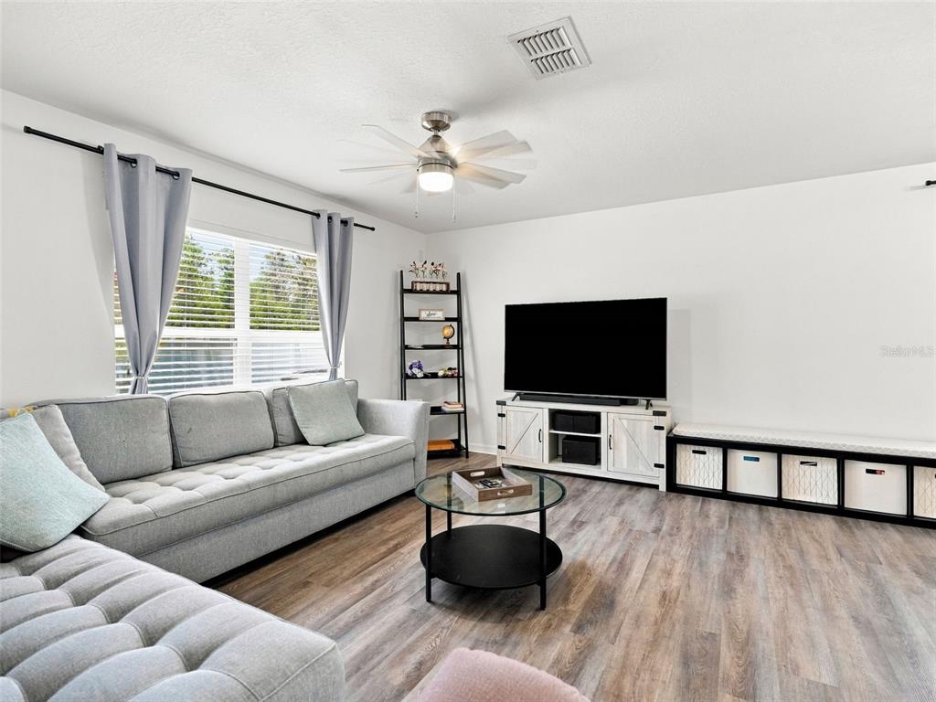 A living room features a grey sectional sofa, a television on a white stand, and wood-look flooring — 12607 CHENWOOD AVENUE, HUDSON, FL