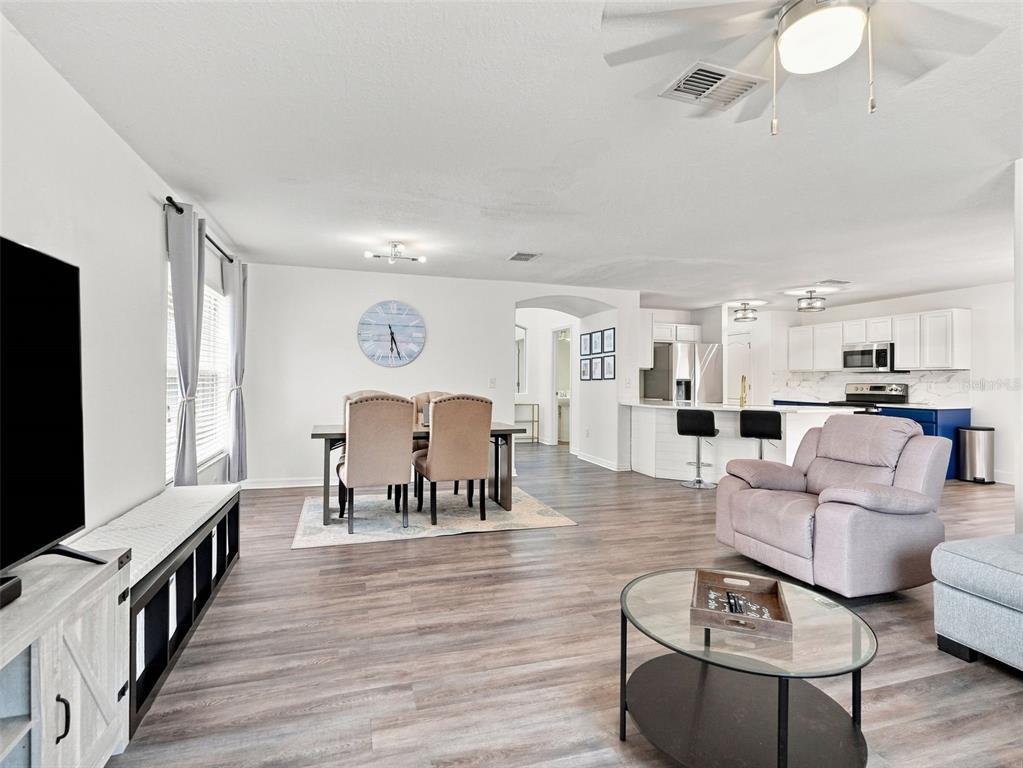 An open-concept living and dining area features wood-look flooring, a kitchen island, and neutral furniture — 12607 CHENWOOD AVENUE, HUDSON, FL