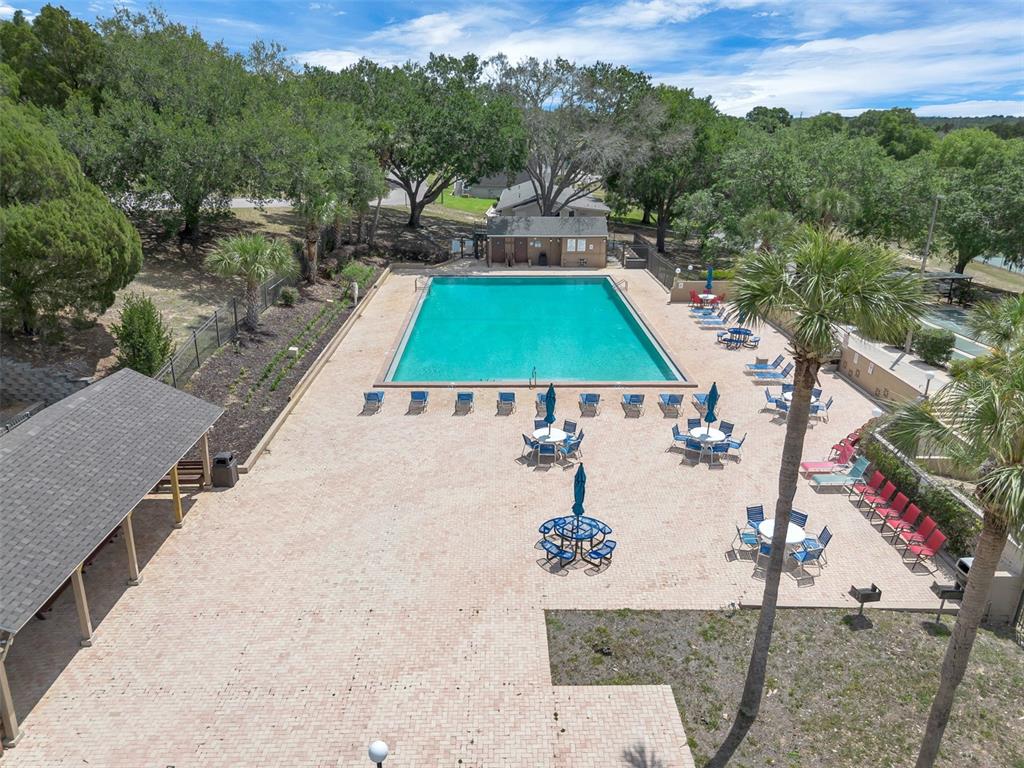 An aerial view shows a rectangular swimming pool surrounded by a paved patio and trees — 10301 US HIGHWAY 27 UNIT 92, CLERMONT, FL