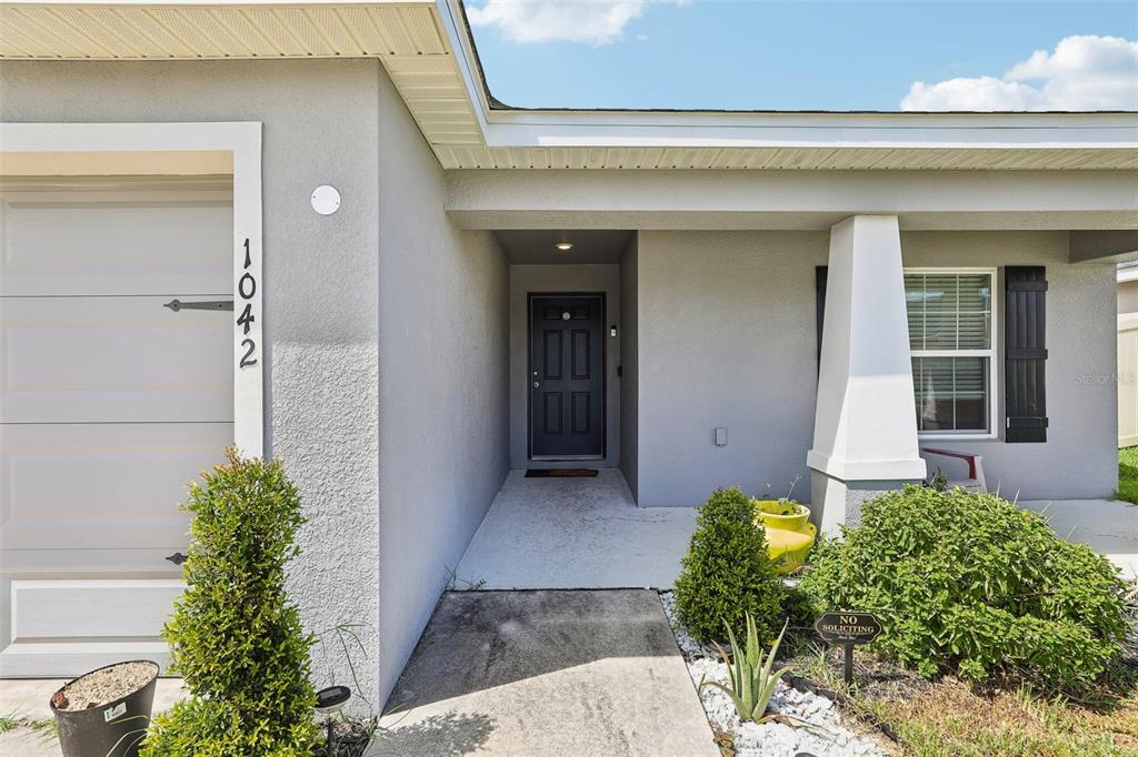 The exterior of a house features a gray stucco facade, a dark front door, and landscaping — 1042 CORSO DR, WINTER HAVEN, FL