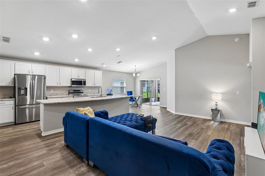 An open-concept kitchen and living area features white cabinetry, stainless steel appliances, and blue furniture — 1042 CORSO DR, WINTER HAVEN, FL