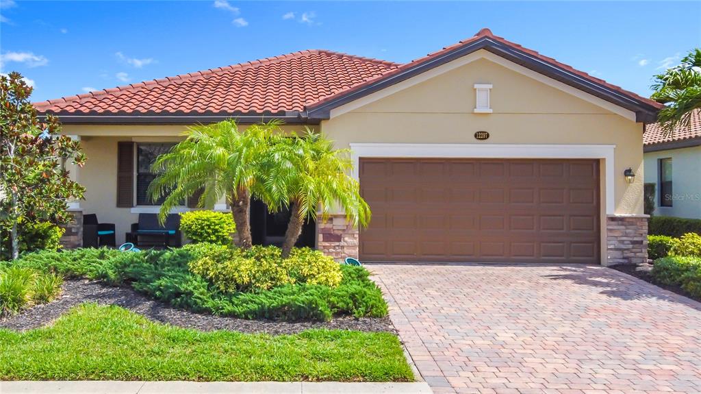 A single-story house with a tiled roof, a two-car garage, and a landscaped front yard — 12297 CANAVESE LANE, VENICE, FL