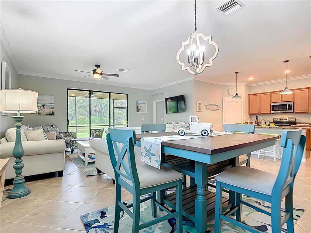 An open-concept living and dining area features a blue wooden dining set and tile flooring — 12297 CANAVESE LANE, VENICE, FL
