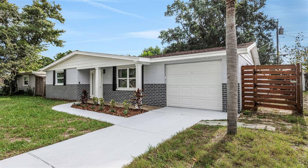A single-story house with a gray brick facade, white garage door, and a wooden side fence — 2332 CHANCERY DRIVE, HOLIDAY, FL