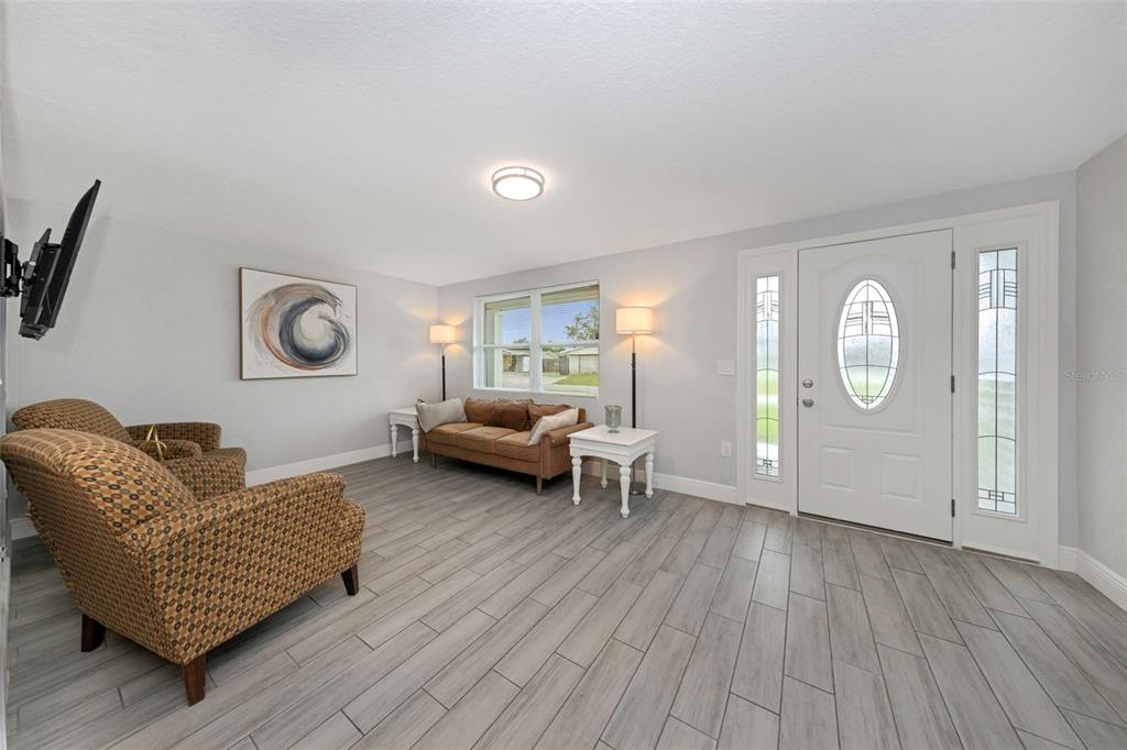 A living room features gray wood-look tile flooring, white walls, and a white front door — 2332 CHANCERY DRIVE, HOLIDAY, FL