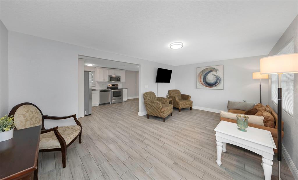 A living room with light wood-look tile flooring opens into a kitchen with white cabinets — 2332 CHANCERY DRIVE, HOLIDAY, FL