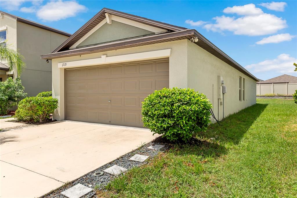 A tan house exterior features a beige garage door and a green shrub in front — 1719 FRED IVES STREET, RUSKIN, FL