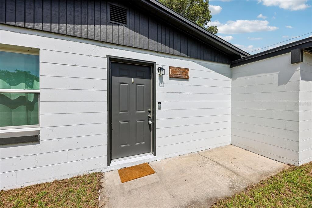 A gray front door is set into a white concrete block wall under a dark roof — 668 BARBUDA WAY, ALTAMONTE SPRINGS, FL
