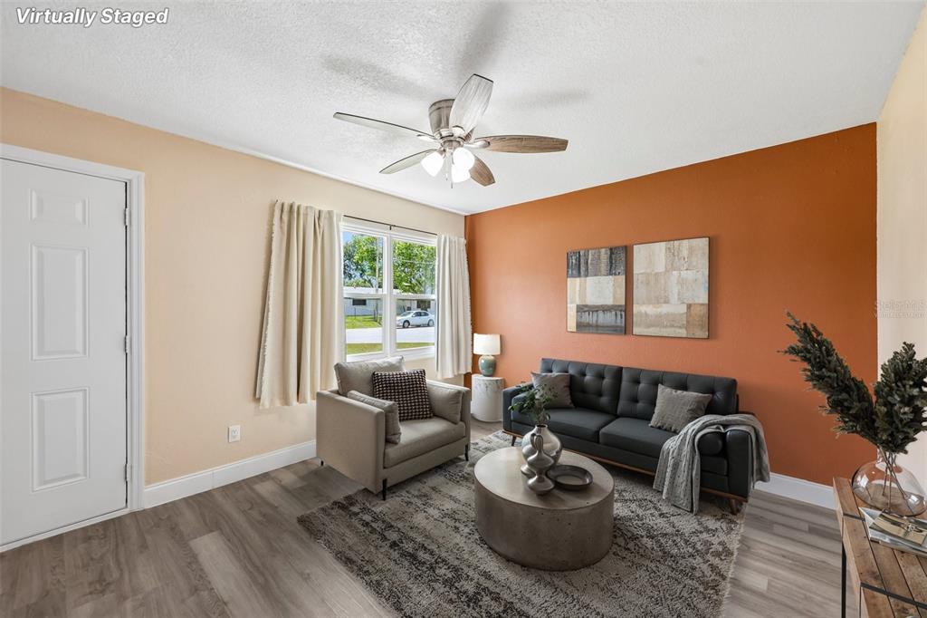 A living room with a burnt orange accent wall, gray sofa, armchair, and wood-look flooring — 668 BARBUDA WAY, ALTAMONTE SPRINGS, FL