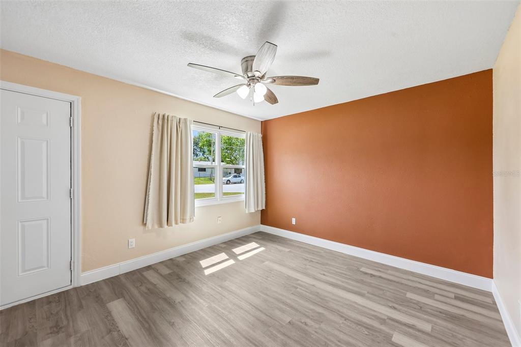 An empty room features light wood-look flooring, a ceiling fan, and an orange accent wall — 668 BARBUDA WAY, ALTAMONTE SPRINGS, FL