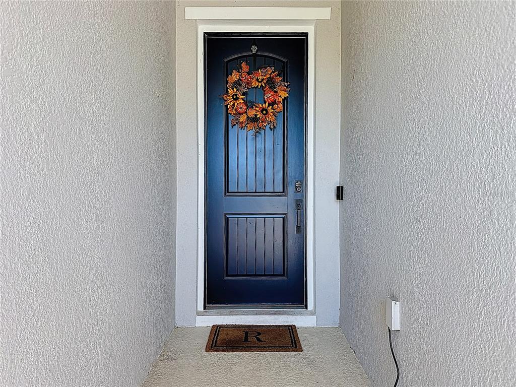A dark blue front door with a fall wreath sits in a recessed entryway — 1404 GERANIUM DRIVE, MASCOTTE, FL