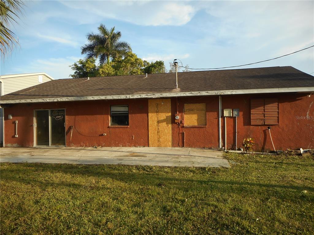 The exterior of a single-story house with red stucco walls, a boarded-up door, and sliding glass doors — 609 1ST AVENUE NW, RUSKIN, FL