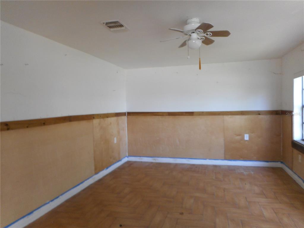 An empty room features wood paneling on the lower walls, white upper walls, and parquet flooring — 609 1ST AVENUE NW, RUSKIN, FL