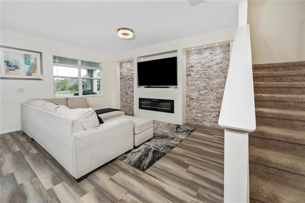 A living room features a stone accent wall, a fireplace, a television, and carpeted stairs — 3107 STONEGATE DRIVE, OCOEE, FL