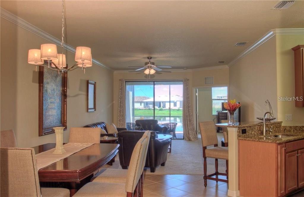 An open-concept dining area and living room with tile floors, a kitchen island, and lake views — 6627 CANDLESTICK DRIVE, BRADENTON, FL