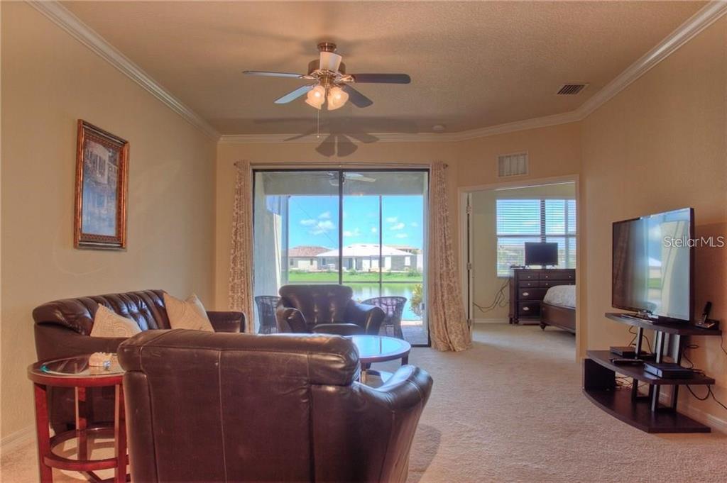 A living room with brown leather furniture, a ceiling fan, and a sliding glass door — 6627 CANDLESTICK DRIVE, BRADENTON, FL