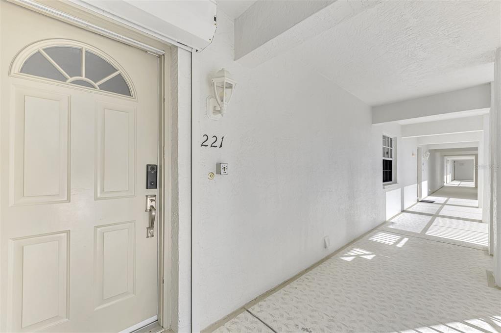 A white front door with a number 221 sign sits in a bright outdoor hallway — 130 BREAKERS COURT UNIT 221, PUNTA GORDA, FL
