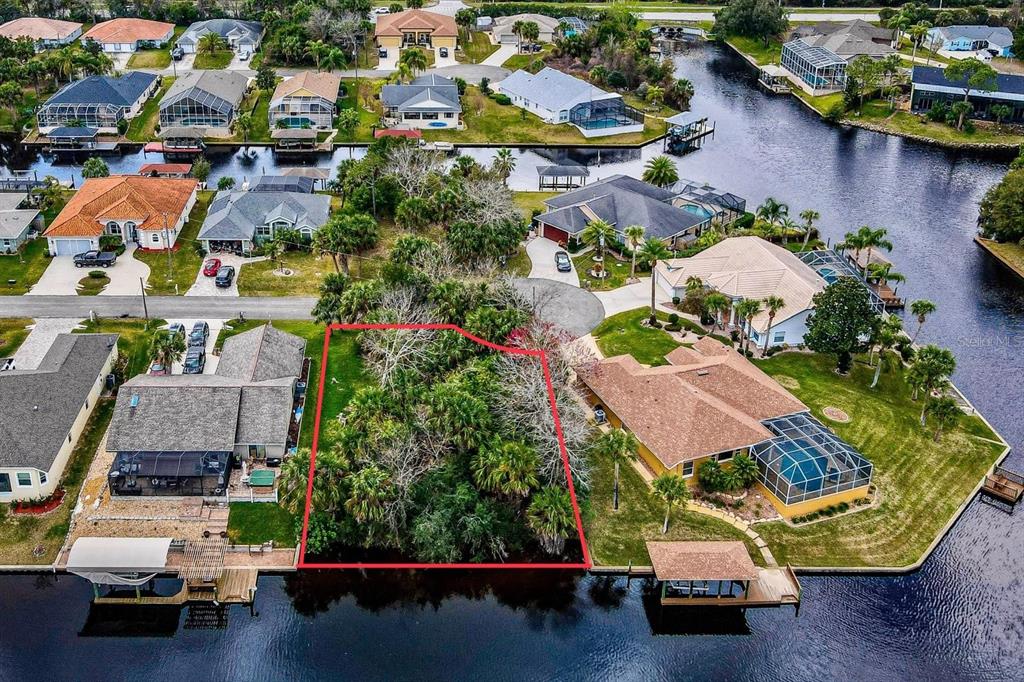 An aerial view shows a vacant, wooded waterfront lot outlined in red between two houses — 16 CRANDON COURT, PALM COAST, FL