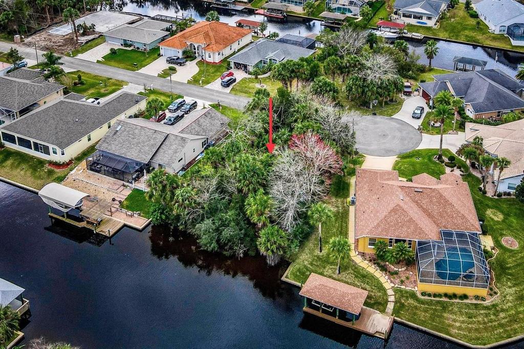 An aerial view shows a vacant, tree-covered residential lot situated between two houses and a canal — 16 CRANDON COURT, PALM COAST, FL