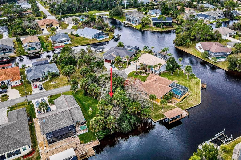 An aerial view shows a residential waterfront lot with a red arrow pointing toward vegetation — 16 CRANDON COURT, PALM COAST, FL