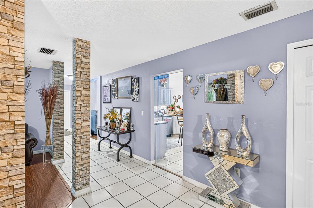 A hallway with tiled floors, stone-clad pillars, and decorative wall accents leads toward a kitchen — 3550 OBERRY ROAD, KISSIMMEE, FL