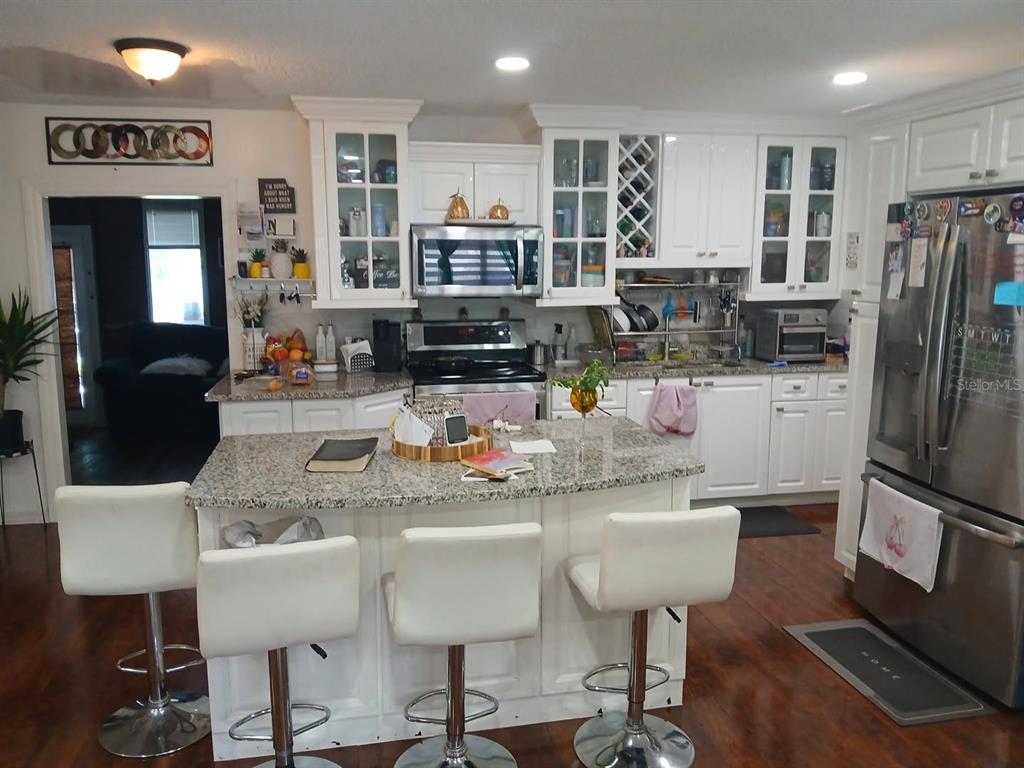 A kitchen with white cabinets, granite countertops, a center island, and three white bar stools — 14342 SE 45TH COURT, SUMMERFIELD, FL