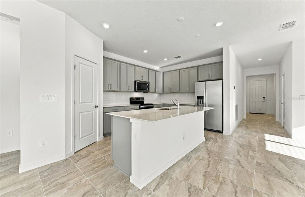 An open-concept living room and kitchen feature light wood floors, white cabinetry, and a sectional — 11116 SYCAMORE GLEN LOOP, THONOTOSASSA, FL