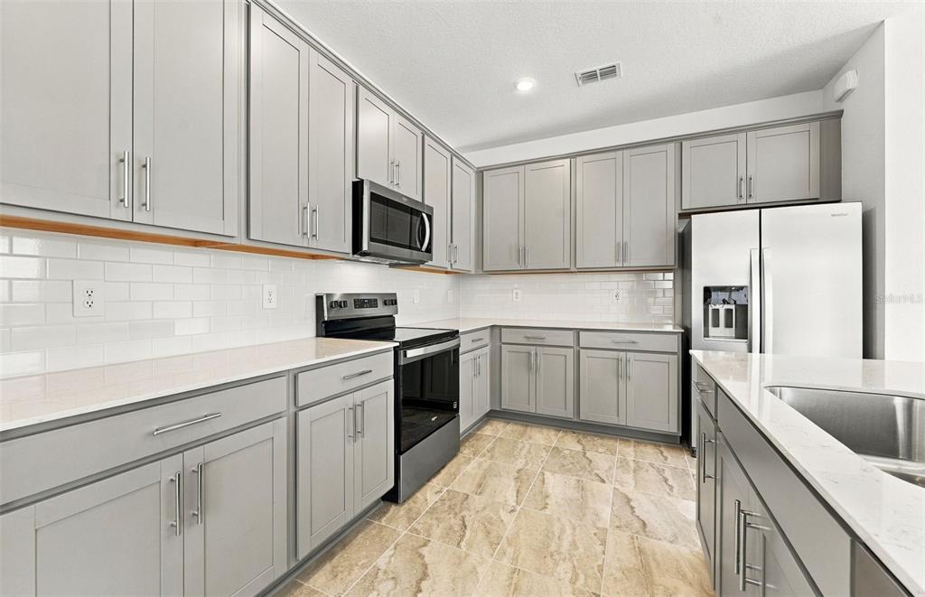 A modern kitchen features white cabinetry, a central island with bar seating, and stainless appliances — 11116 SYCAMORE GLEN LOOP, THONOTOSASSA, FL