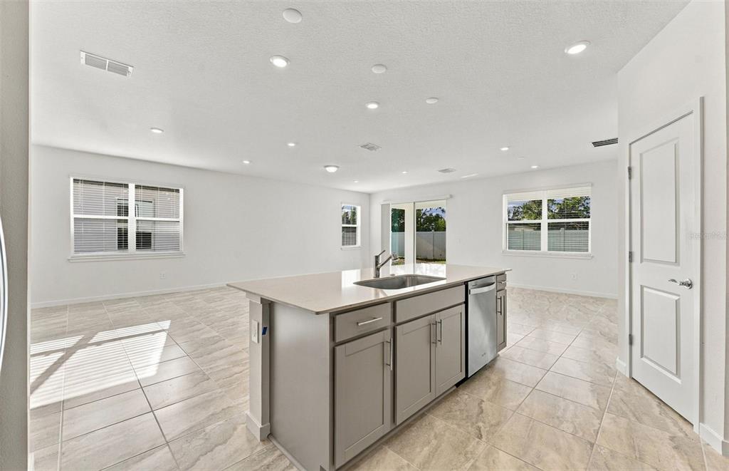 A modern kitchen features white cabinetry, stainless steel appliances, a quartz island, and wood flooring — 11116 SYCAMORE GLEN LOOP, THONOTOSASSA, FL