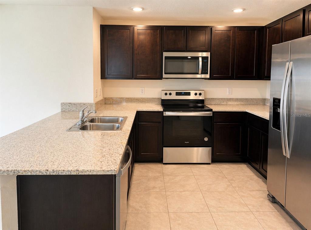 A kitchen features dark wood cabinets, granite countertops, stainless steel appliances, and tile flooring — 16511 MOSAIC OAR DRIVE, WIMAUMA, FL
