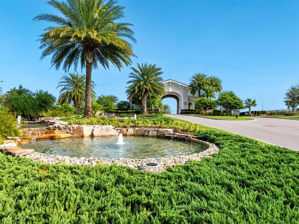 A landscaped entrance features a stone-lined pond with a fountain and a gated archway — 16717 BWANA PLACE, BRADENTON, FL