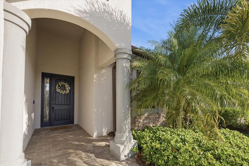 A covered entryway features a dark front door, stone accents, and a large palm tree — 16717 BWANA PLACE, BRADENTON, FL