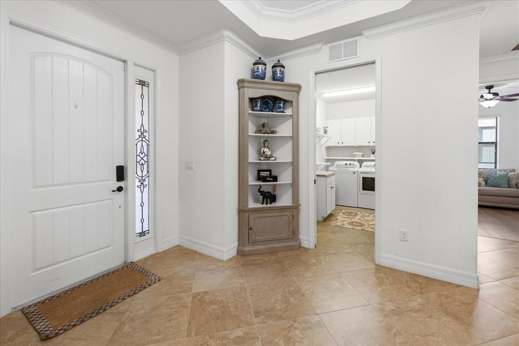 A tiled entryway features a white front door, a corner display shelf, and a laundry room — 16717 BWANA PLACE, BRADENTON, FL