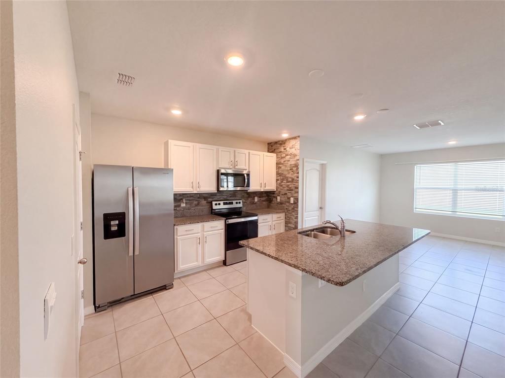 A kitchen with white cabinets, stainless steel appliances, granite countertops, and a central island — 2112 ELIO RIDGE DRIVE, ZELLWOOD, FL