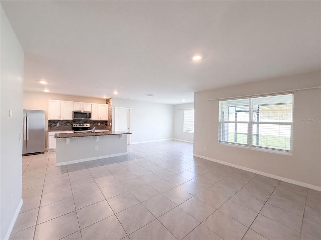 An open-concept kitchen with white cabinets and a breakfast bar overlooks a tiled living area — 2112 ELIO RIDGE DRIVE, ZELLWOOD, FL