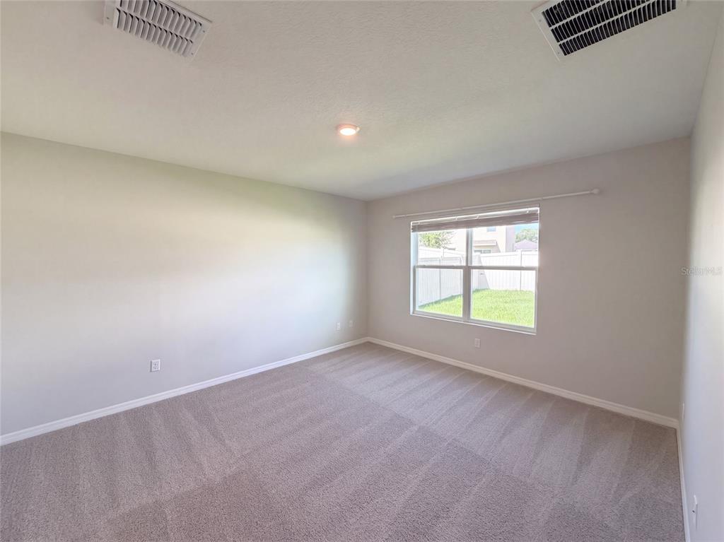 An empty bedroom features light gray walls, beige carpeting, and a single window — 2112 ELIO RIDGE DRIVE, ZELLWOOD, FL