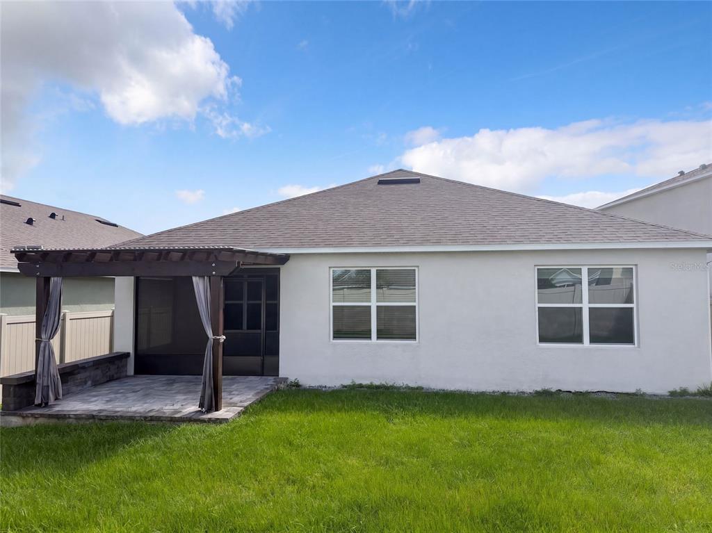 The exterior rear view of a house features a paved patio with a wooden pergola — 2112 ELIO RIDGE DRIVE, ZELLWOOD, FL