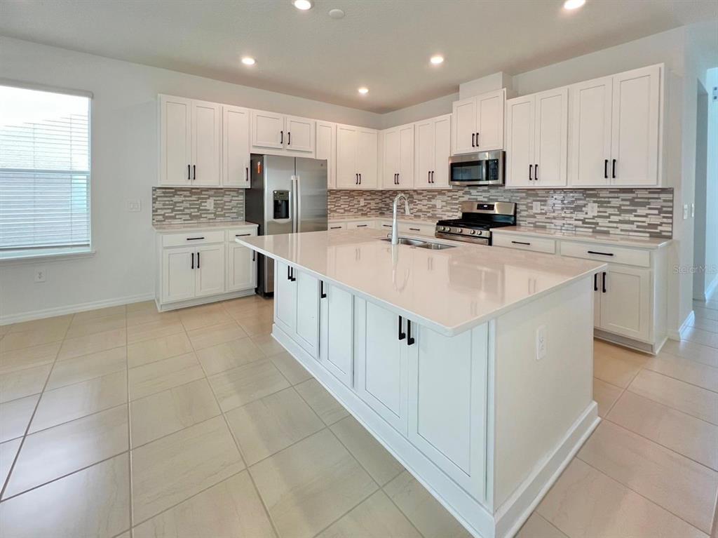 A modern kitchen features white cabinets, a large central island, and stainless steel appliances — 16319 HONEY HARVEST STREET, WINTER GARDEN, FL