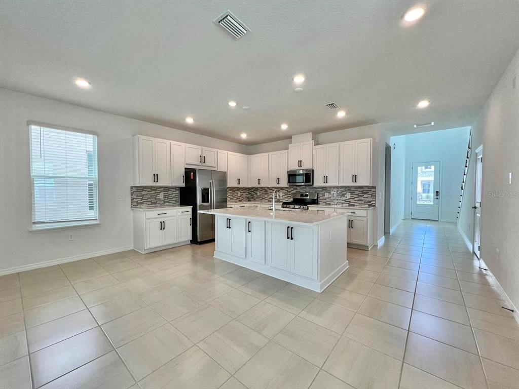 A kitchen with white cabinets, a center island, stainless steel appliances, and light tile flooring — 16319 HONEY HARVEST STREET, WINTER GARDEN, FL