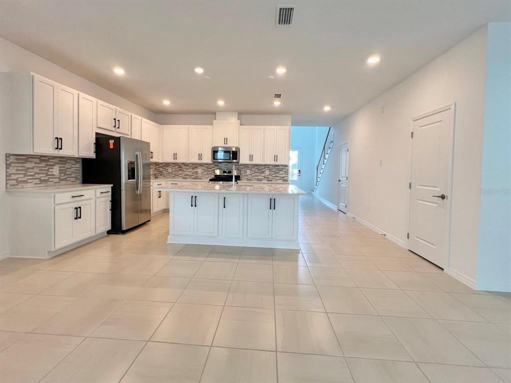 A modern kitchen features white cabinetry, a central island, stainless steel appliances, and tile flooring — 16319 HONEY HARVEST STREET, WINTER GARDEN, FL