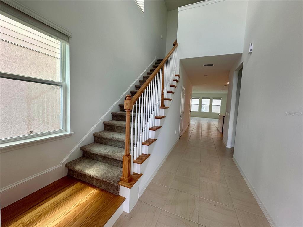 A carpeted staircase with a wooden handrail sits beside a tiled hallway in a home — 16319 HONEY HARVEST STREET, WINTER GARDEN, FL