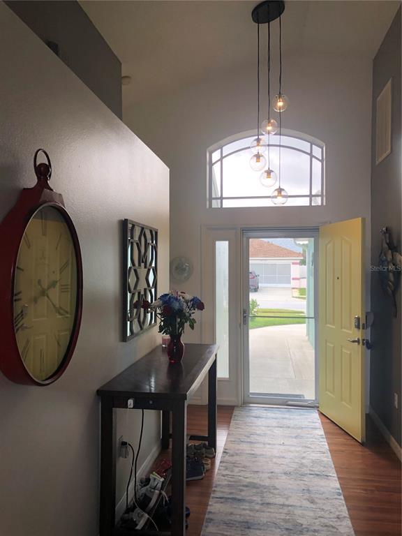 A bright entryway features a yellow front door, a tall clock, and a modern pendant light — 10125 PEOPLES LOOP, PORT RICHEY, FL